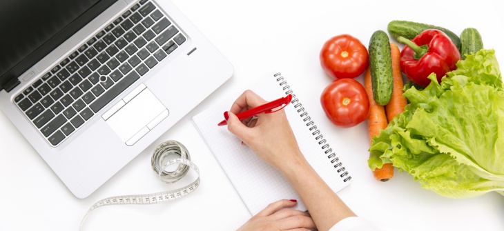 Vegetable diet nutrition or medicaments concept. Doctors hands writing diet plan, ripe vegetable composition, laptop and measuring tape on white background